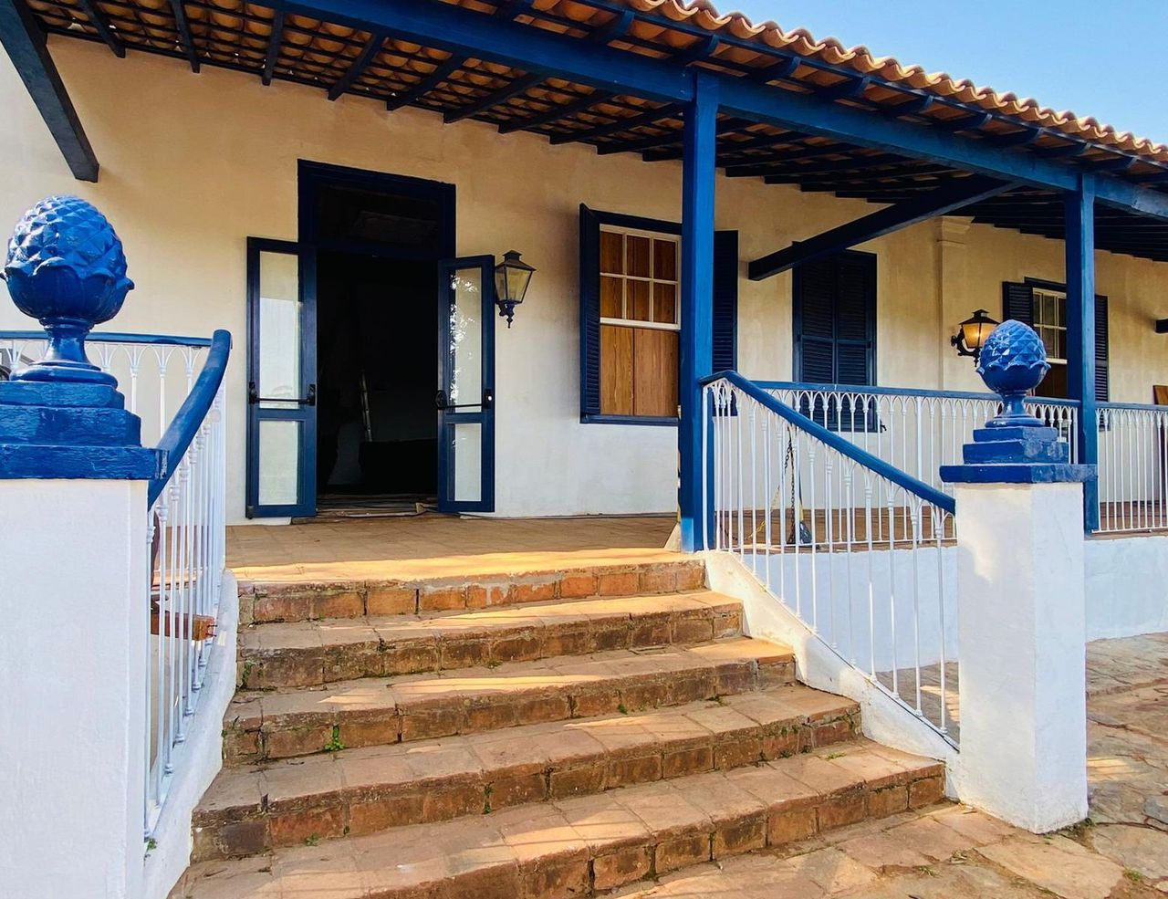 Foto da escadaria e da entrada do casarão restaurado, com portas e pinhas azuis