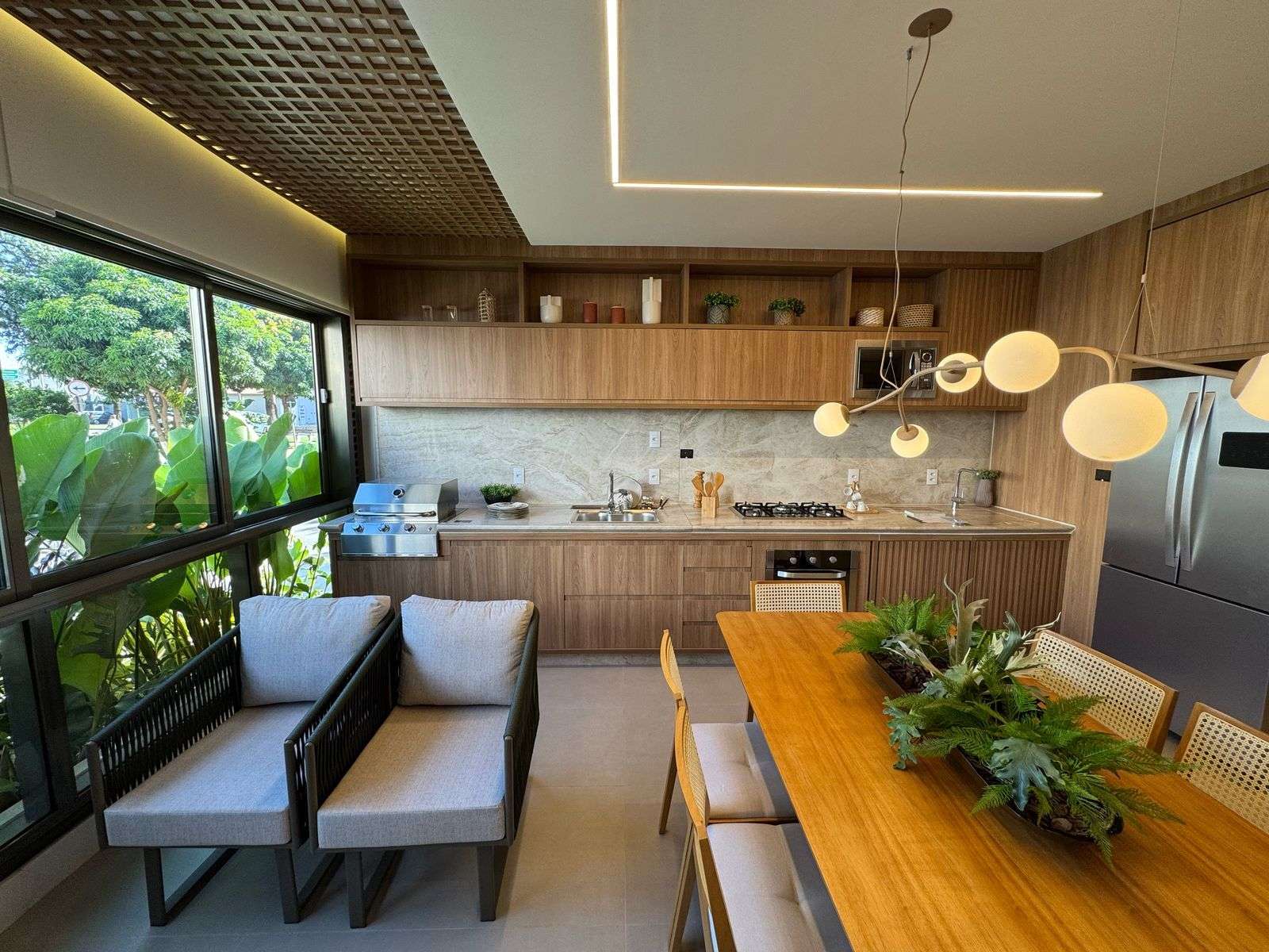 Vista da cozinha do decorado para a varanda envidraçada com poltronas e vegetação do lado de fora