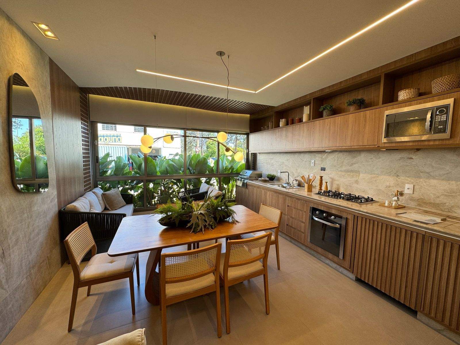Cozinha do decorado com bancada em pedra clara, cooktop, forno embutido, micro-ondas e mesa de jantar junto à janela