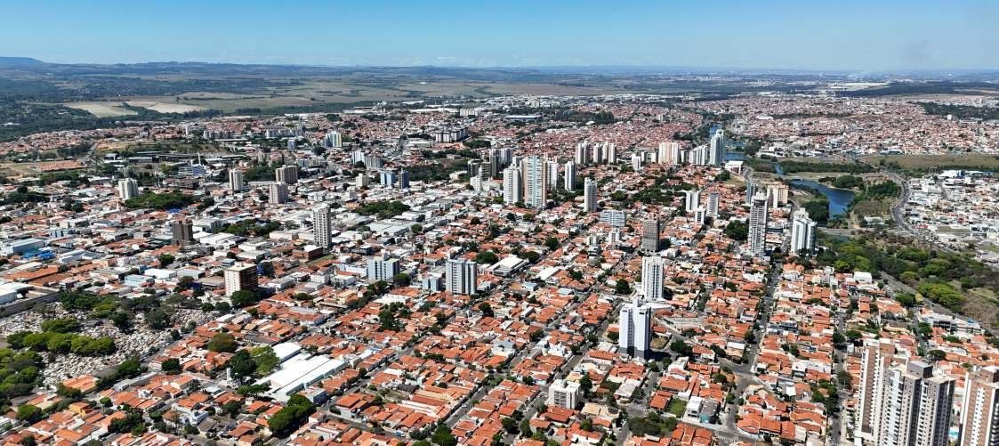 Foto aérea do Centro de Indaiatuba, com casas de telhado cerâmico, prédios e a área verde e o lago do Parque Ecológico à direita