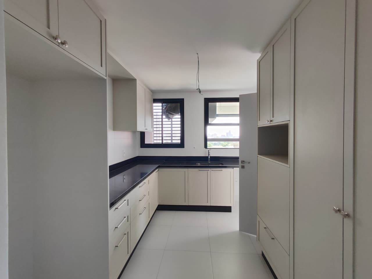 Foto real da cozinha em L do apartamento 44, com armários claros, bancada escura com cuba e torre de armários com nicho