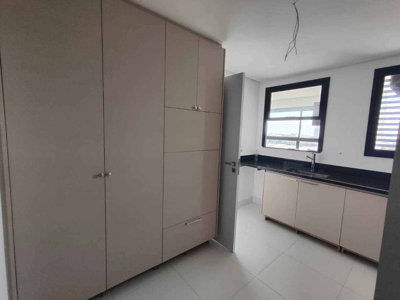 Foto real da cozinha do apartamento 33, com paredão de armários claros, bancada escura com cuba e janela