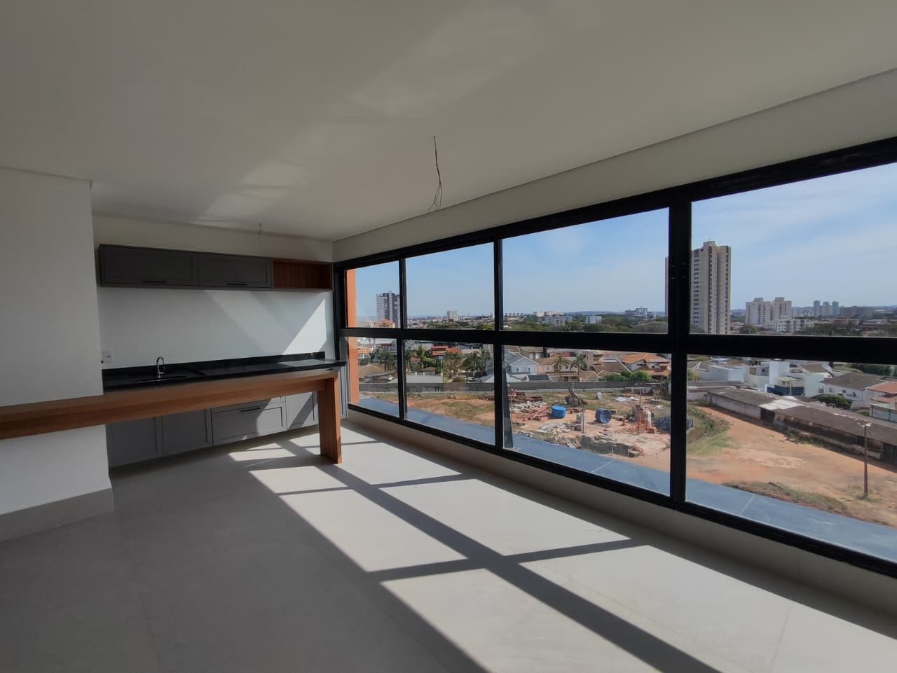 Foto real do espaço gourmet do apartamento 44, com cuba em bancada escura, armários cinza e balcão de madeira junto à janela