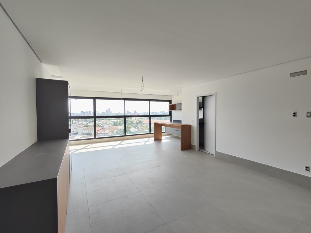 Foto real do living do apartamento 33, com aparador cinza à esquerda, balcão de madeira junto à janela e piso em placas claras