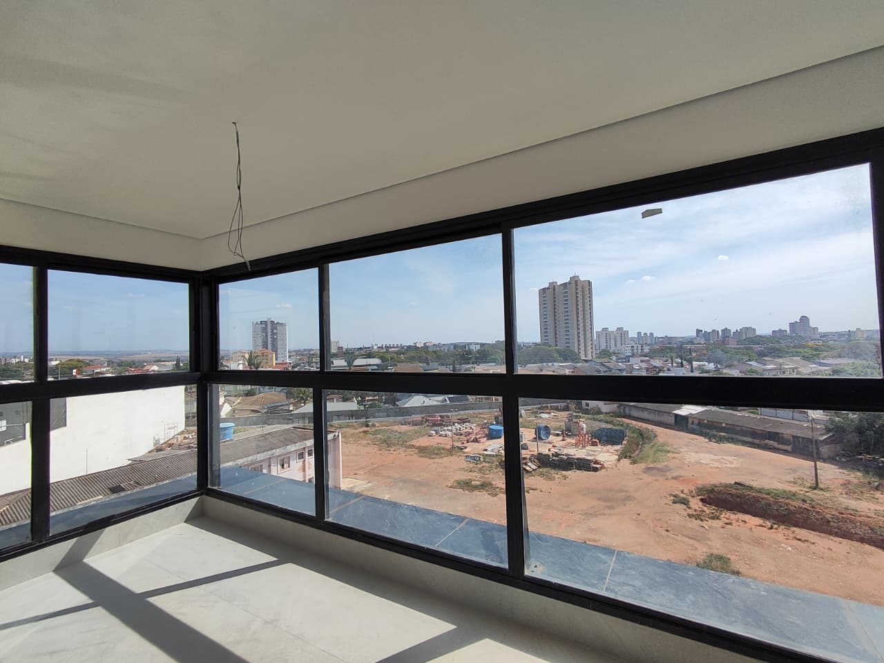Foto real do canto do living do apartamento 33 do Reserva Luiza Tomaselli, com janelas em L de caixilho preto, prédios da cidade ao fundo e um terreno em obra logo abaixo