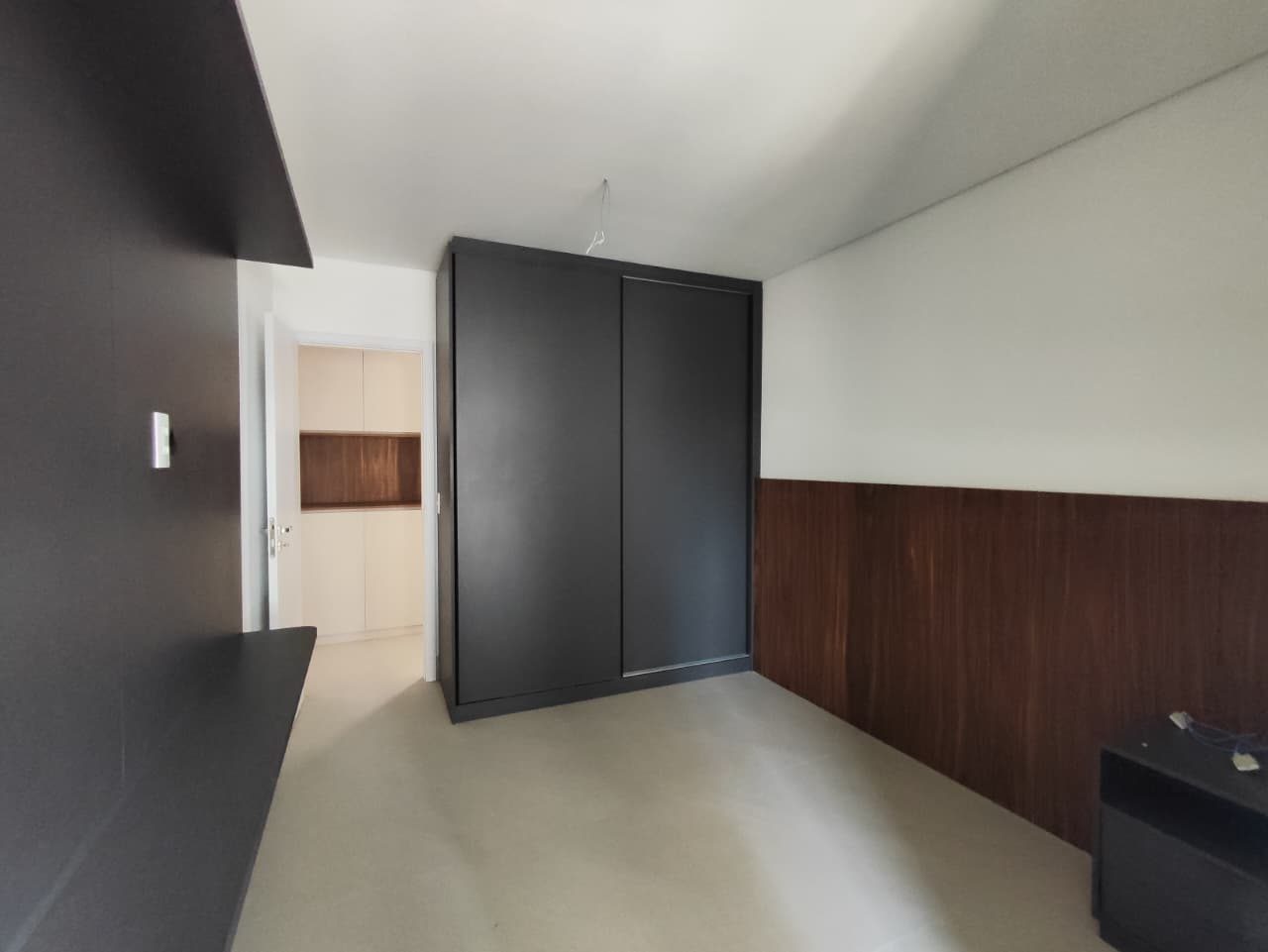 Foto real de uma suíte do apartamento 44, com armário de portas de correr escuro, painel de madeira na parede e bancada